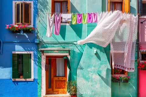 A very colorful house with clean laundry hanging and blowing in the wind on the island of Burano, Italy.